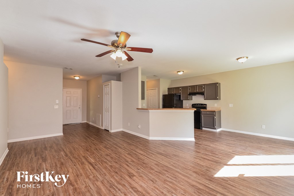 an empty living room with a ceiling fan and a kitchen
