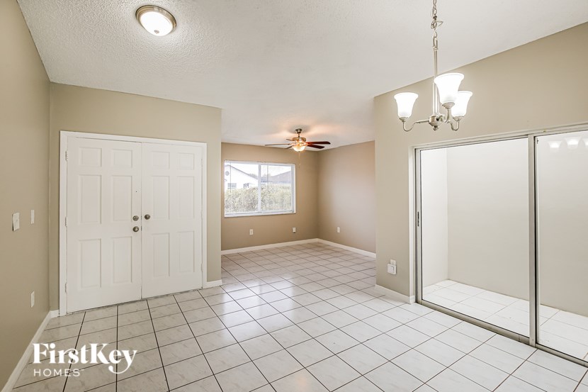A spacious room with a white door, a ceiling fan, and a chandelier.