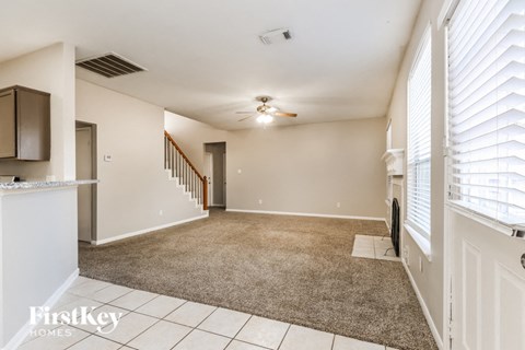 A spacious room with a carpeted floor and a staircase in the background.