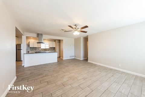 A spacious room with a ceiling fan and light fixture, and a kitchen area with a stove and refrigerator in the background.
