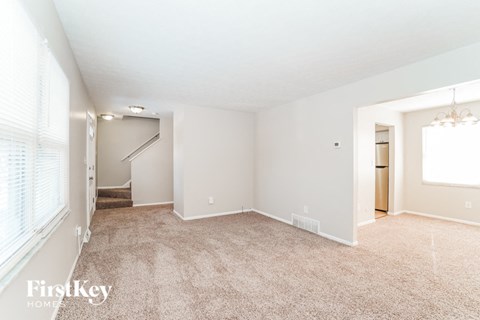 A spacious room with a carpeted floor and a staircase leading to another room.