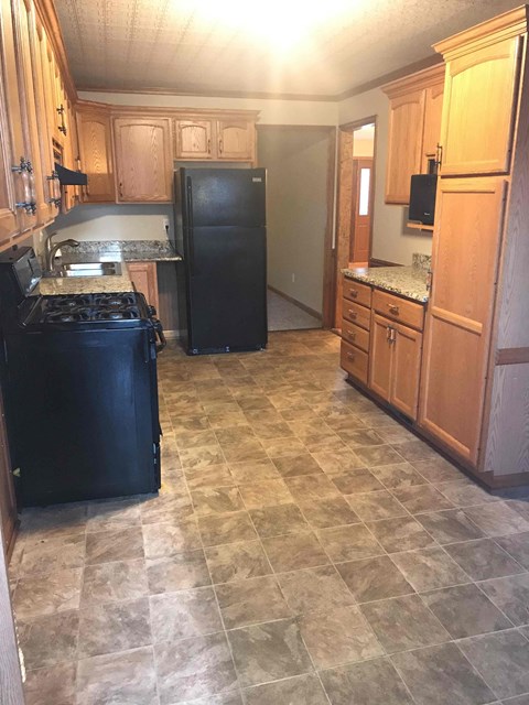 A kitchen with a black refrigerator and wooden cabinets.