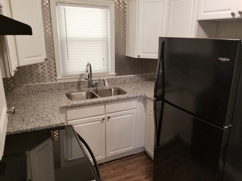 A black refrigerator sits in a kitchen with white cabinets.