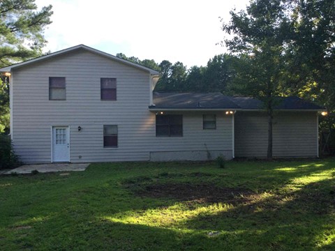 A house with a white door and windows is surrounded by trees.