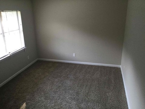 A room with a carpeted floor and a window with blinds.