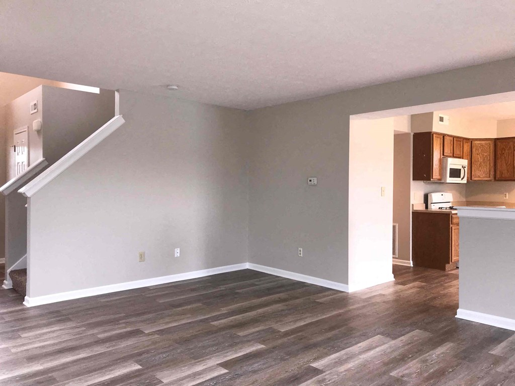 an empty living room with wood floors and a kitchen