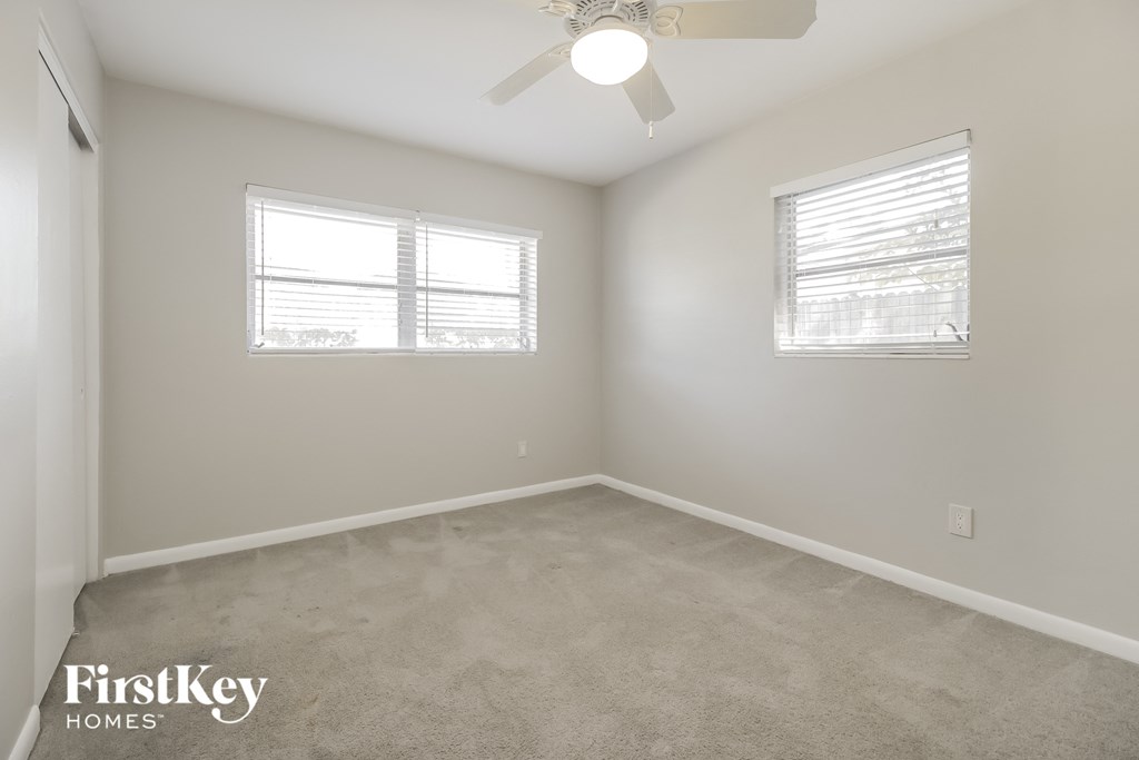 an empty room with two windows and a ceiling fan