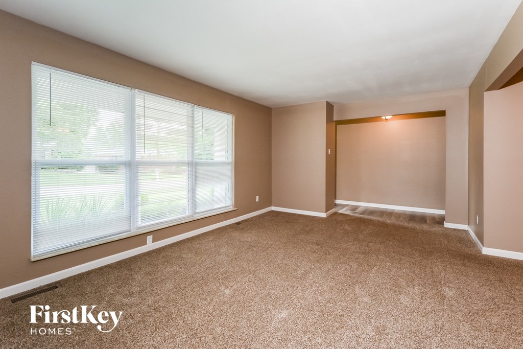 an empty living room with large windows and carpet