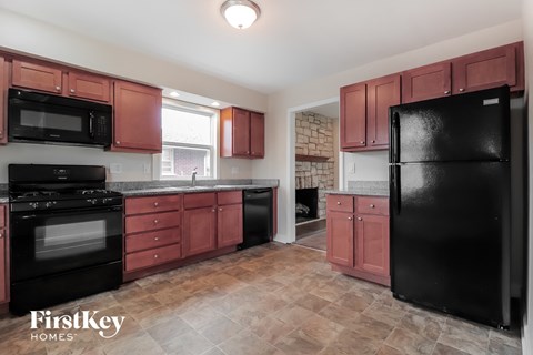 A kitchen with red cabinets and black appliances.