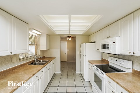 A kitchen with white cabinets and appliances, a sink, and a refrigerator.