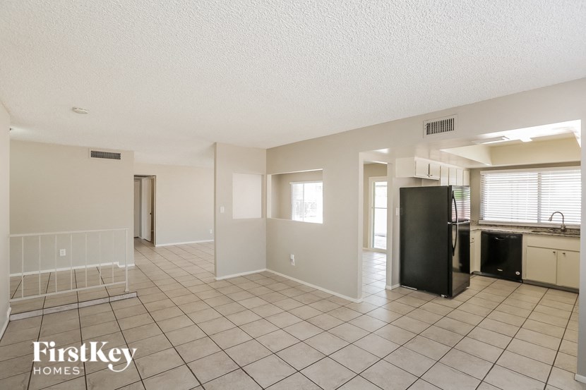 an empty kitchen and living room with tile flooring and a refrigerator