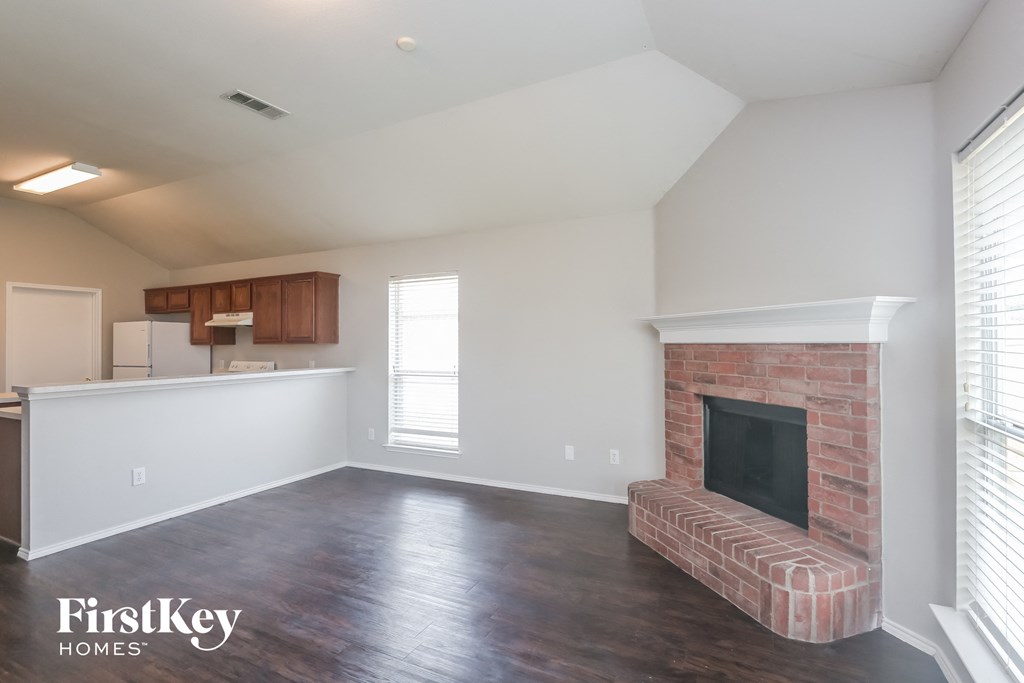 A large empty room with a fireplace and wooden floors.