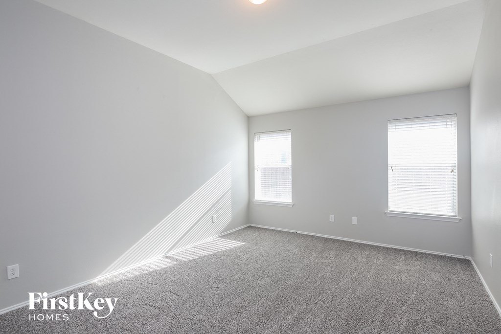 A sparsely furnished room with a carpeted floor and two windows.