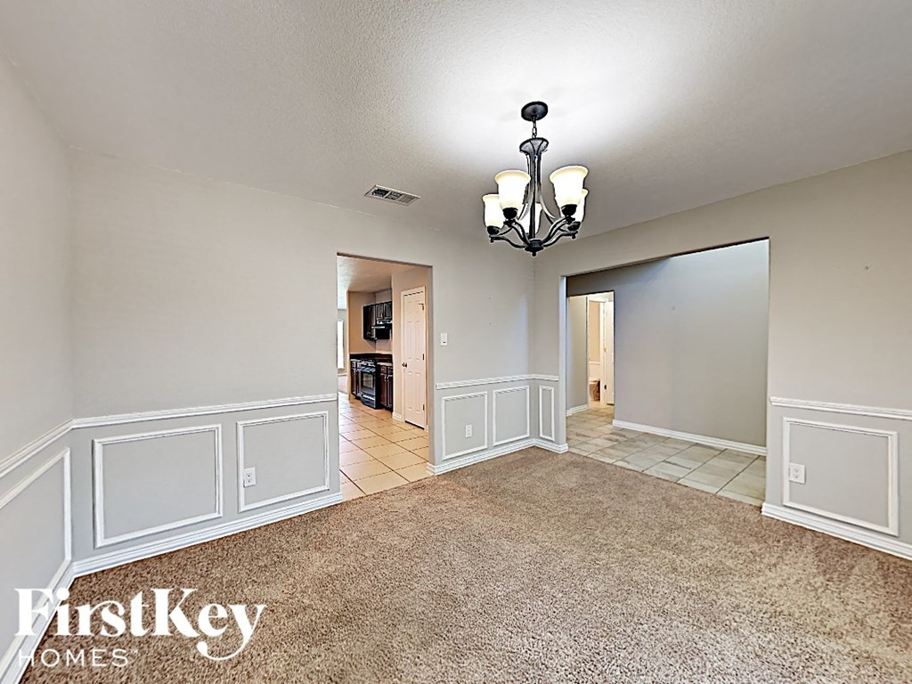 A spacious room with a chandelier and a carpeted floor.