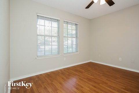 a bedroom with wood floors and two windows and a ceiling fan