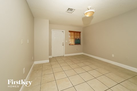 A spacious room with beige walls and tile flooring, featuring a door and a window with blinds.