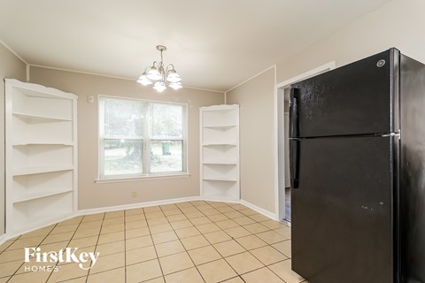 A black refrigerator is in a kitchen with white cabinets and a tile floor.