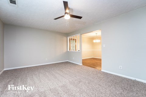 A spacious room with a carpeted floor and a ceiling fan.