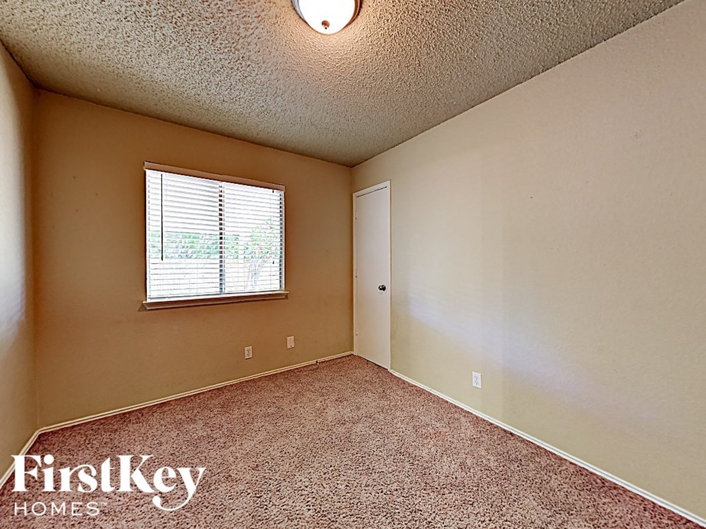 A room with a carpeted floor and a window with blinds.
