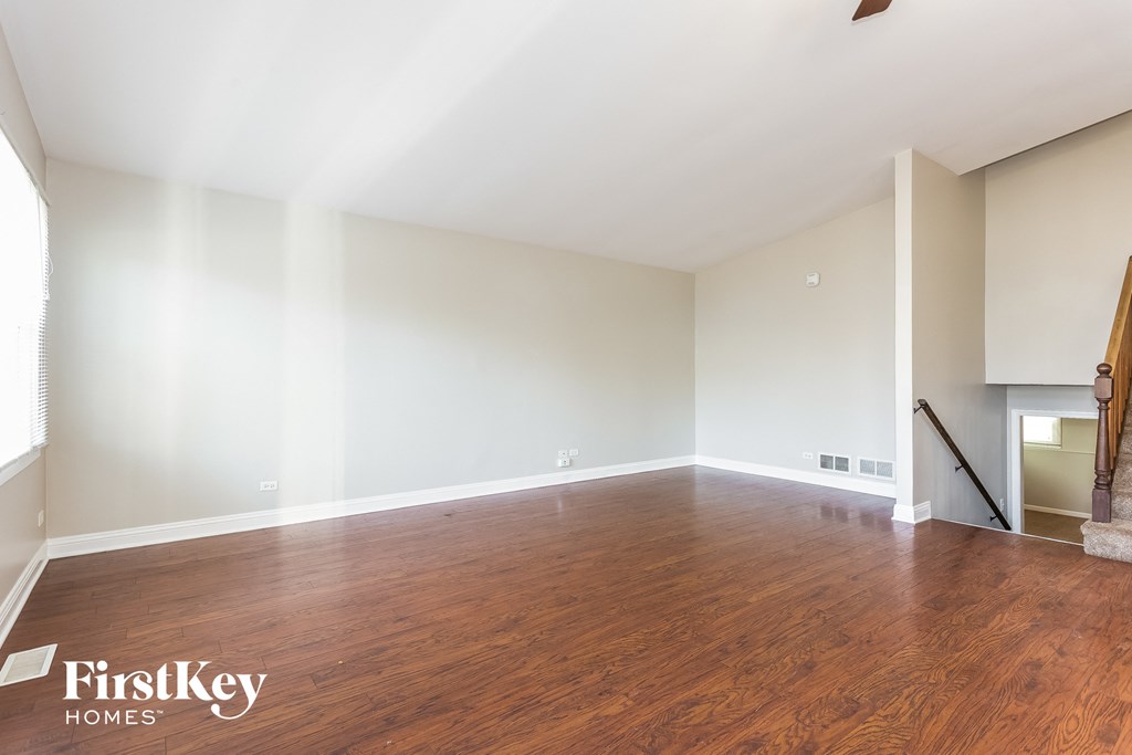 A spacious room with wooden floors and a staircase on the right side.
