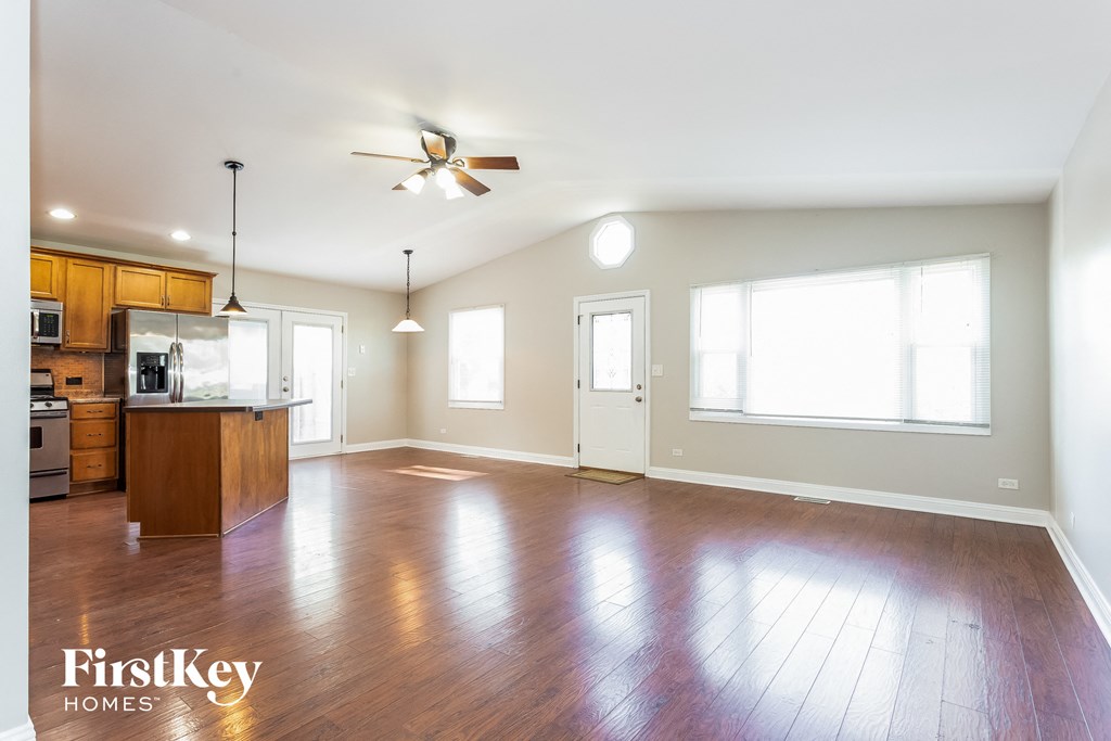 A spacious kitchen and living room with wooden floors and a ceiling fan.