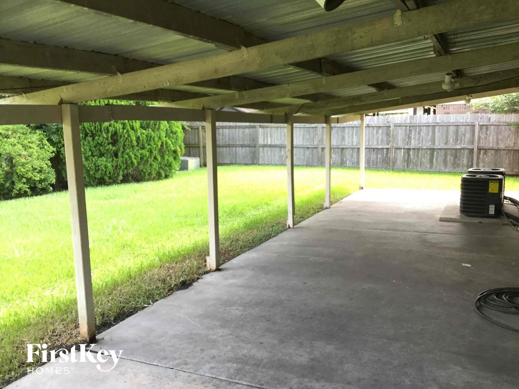 a covered patio with grass and a trash can