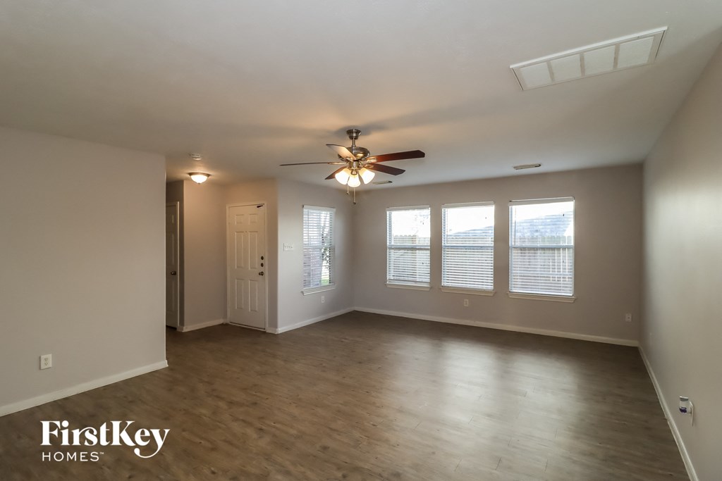 an empty living room with a ceiling fan and windows