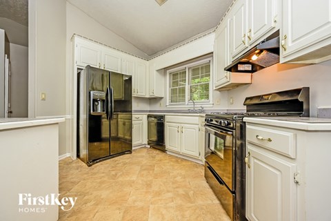 A kitchen with a black fridge and stove and white cabinets.