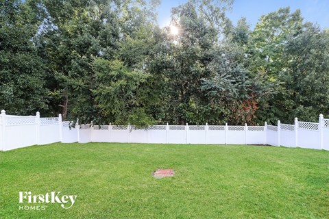 A white fence encloses a green lawn with trees in the background.