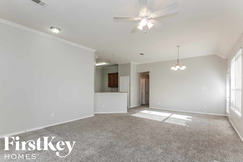 an empty living room with a ceiling fan and a kitchen
