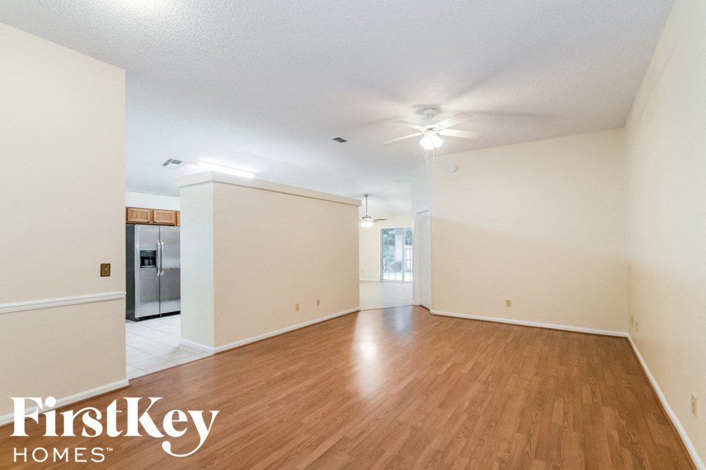 A spacious room with wooden floors and a refrigerator in the corner.