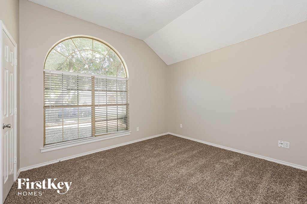 A room with a carpeted floor and a large arched window with blinds.