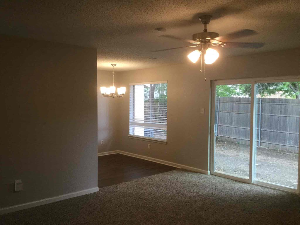 an empty living room with a ceiling fan and a sliding glass door