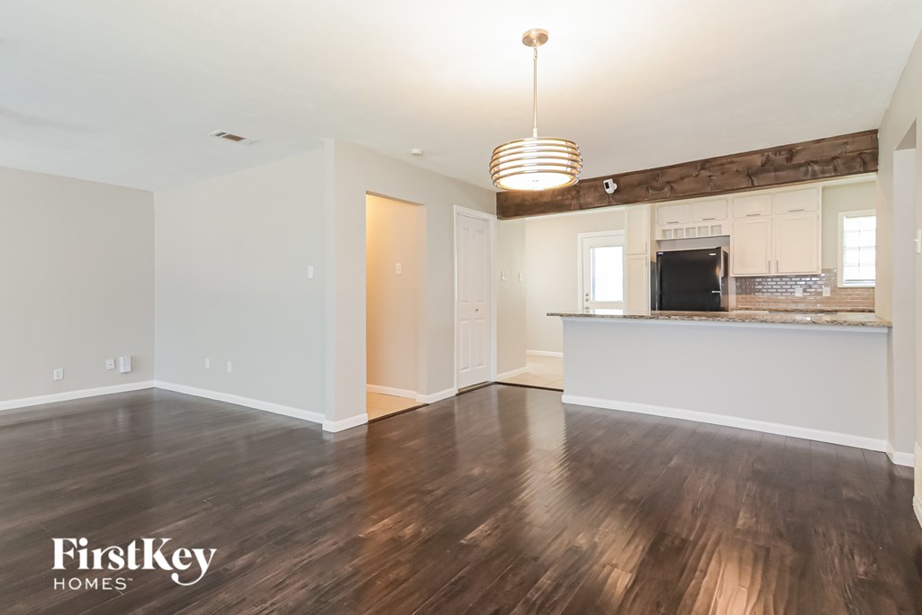 A spacious room with wooden floors and a kitchen area in the background.