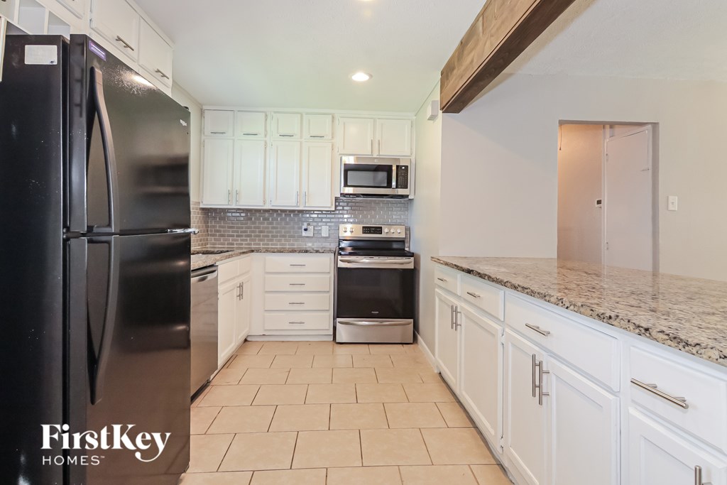 A kitchen with a black fridge and white cabinets.