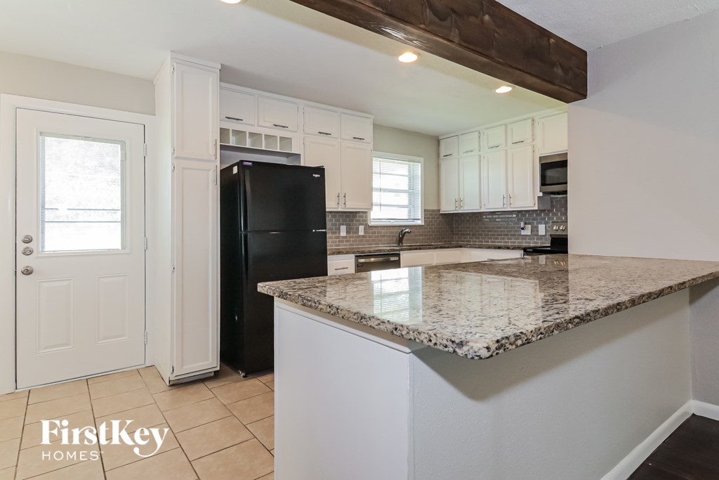 A kitchen with a black fridge and a granite counter top.