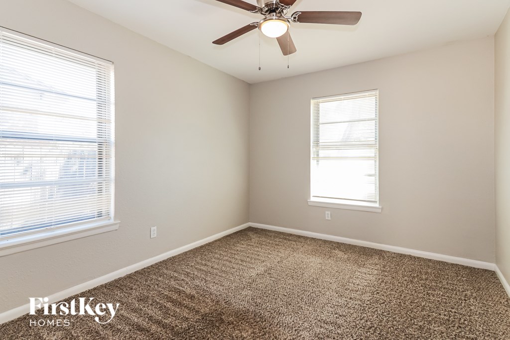 A room with a carpeted floor, a ceiling fan, and a window with blinds.
