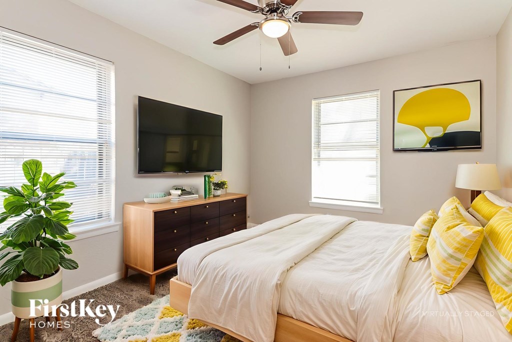 A bedroom with a bed, a dresser, a ceiling fan, and a television.