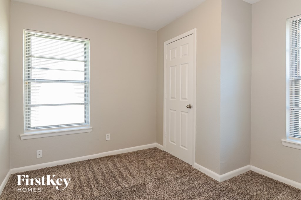 A room with a carpeted floor, a door, and a window with blinds.