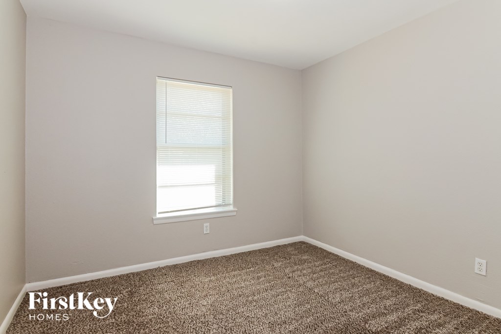 A room with a carpeted floor and a window with blinds.