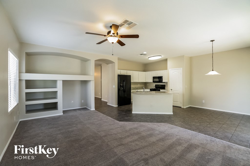 an empty living room with a ceiling fan and a kitchen
