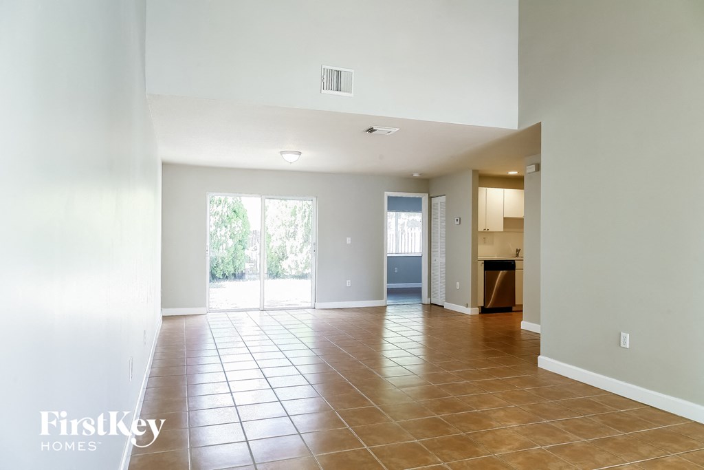an empty living room with a sliding glass door to a kitchen
