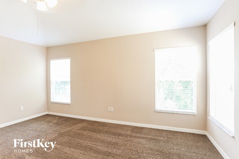 a spacious living room with carpet and two windows