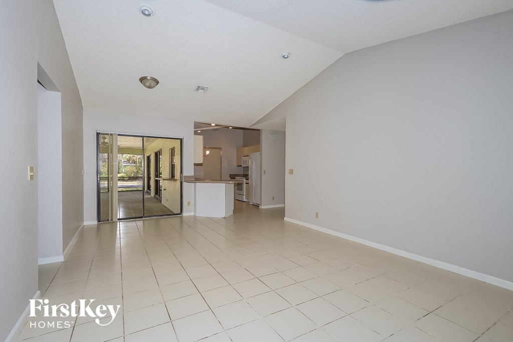 a spacious living room and kitchen with white tiled flooring and white walls