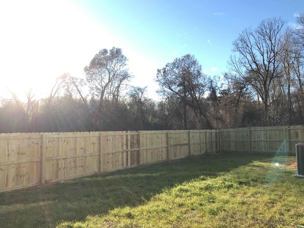 A wooden fence surrounds a grassy area with trees in the background.