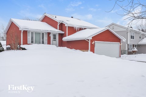 A red house with a white garage door in the snow.