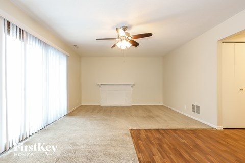 A spacious room with a ceiling fan and a large window with curtains.