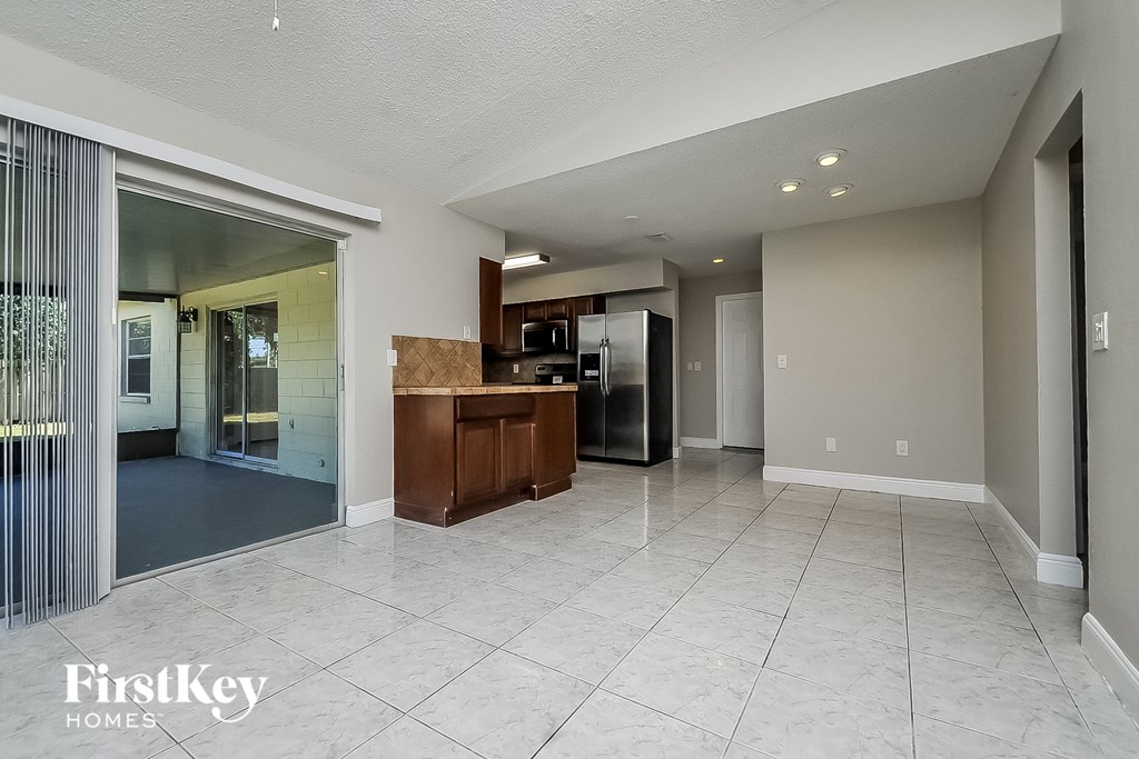 a spacious living room with a kitchen with a stainless steel refrigerator