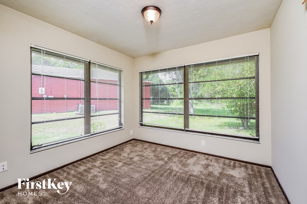 the living room of an apartment with two large windows and carpeting