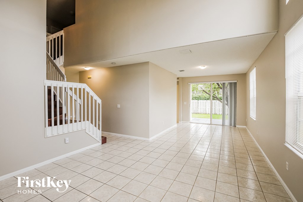 A spacious room with a staircase on the left and a sliding glass door on the right.